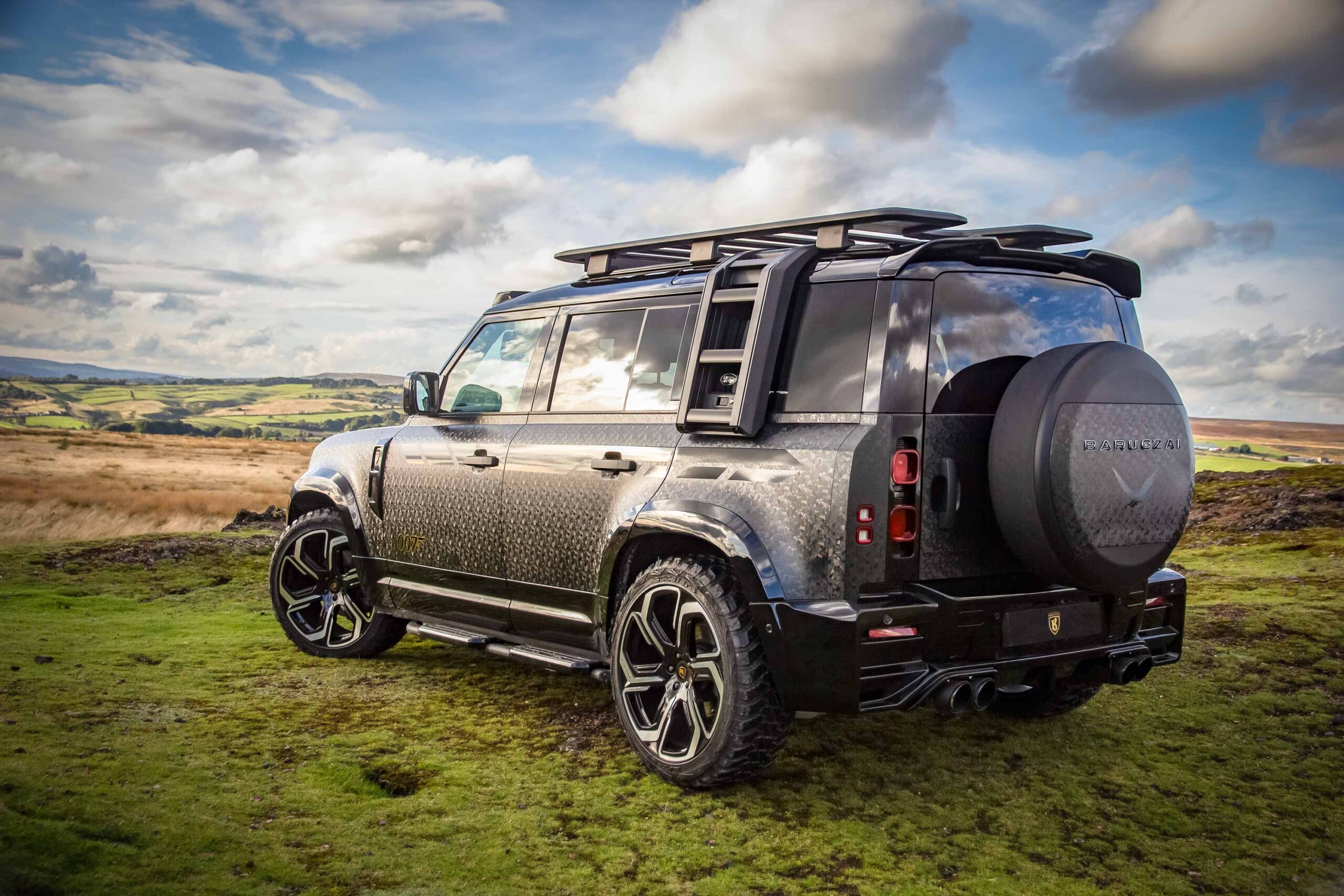 Rear quarter view of a custom wrapped Land Rover Defender 110 L663 2020+. Shot outside near mountains. Fitted with Barugzai Sabre 22” alloy wheels, in Gloss Black Polished Face.