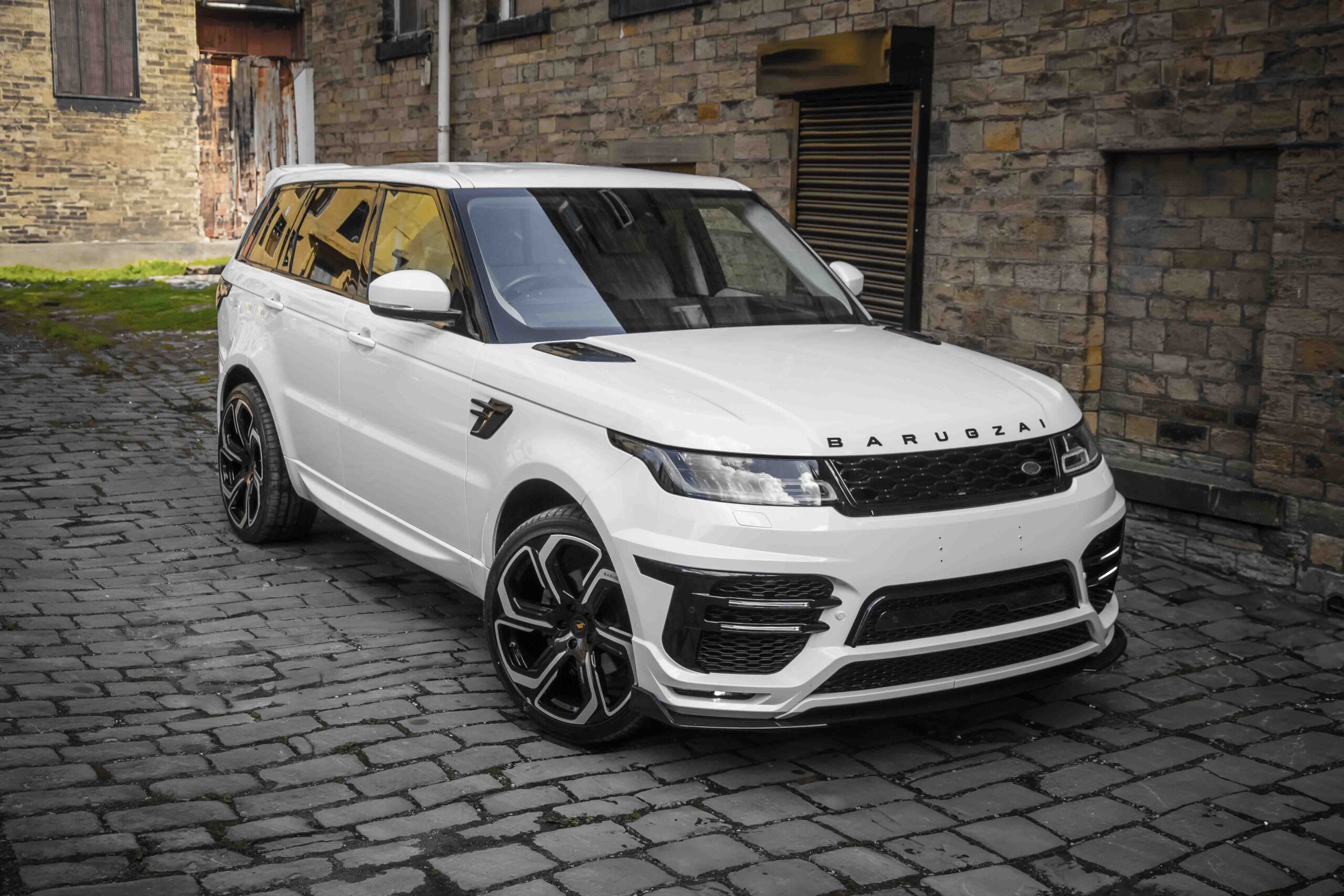Front quarter view of a White Range Rover Sport L494 2018-2022. Shot outside an old mill. Fitted with Barugzai Sabre 22” alloy wheels, in Gloss Black Polished Face.