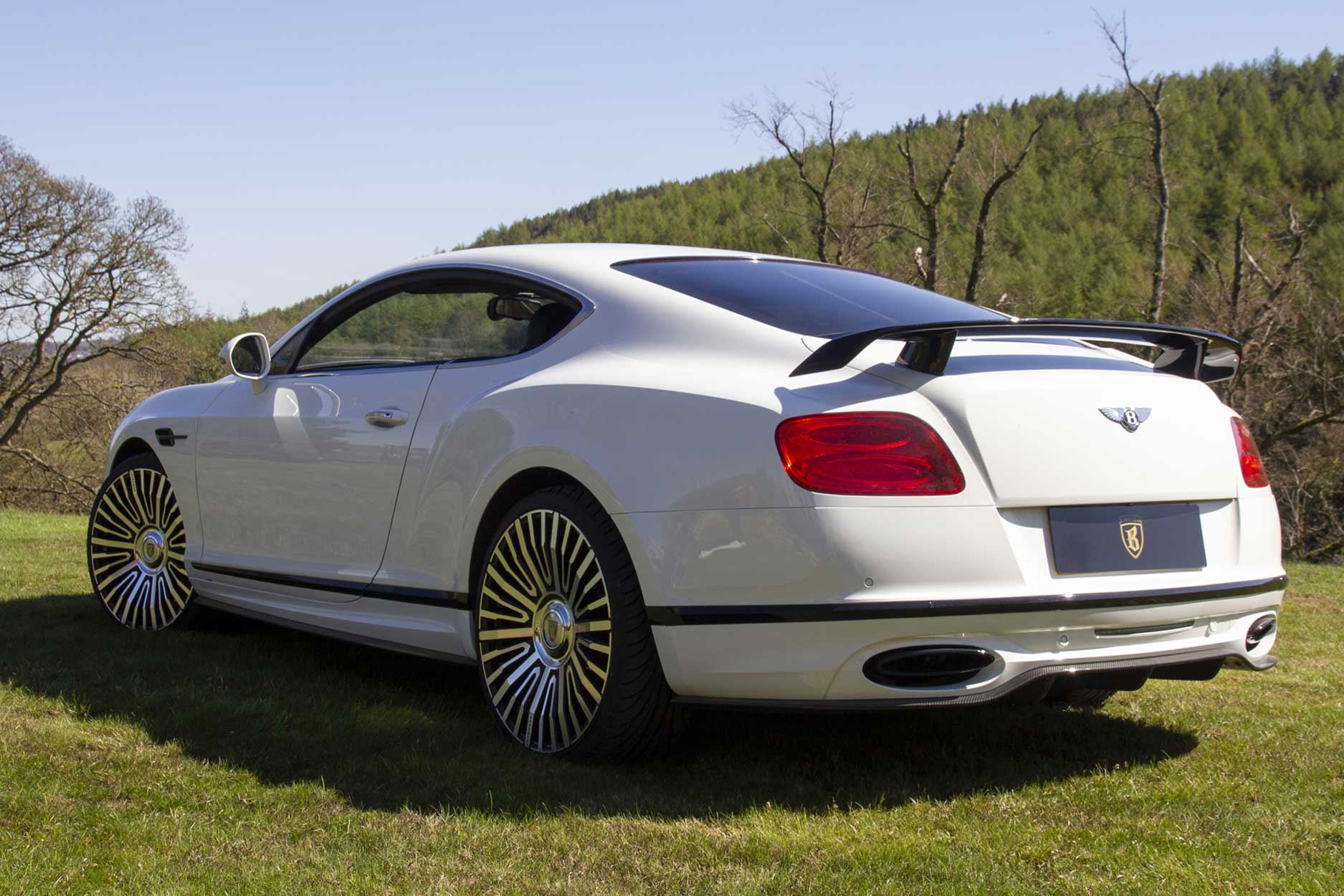 Alt text: Rear quarter view of a White Bentley Continental GT 2018. Shot outside a scenic mansion. Fitted with Barugzai Casanova 22/23” alloy wheels, in Gloss Black Polished Face.