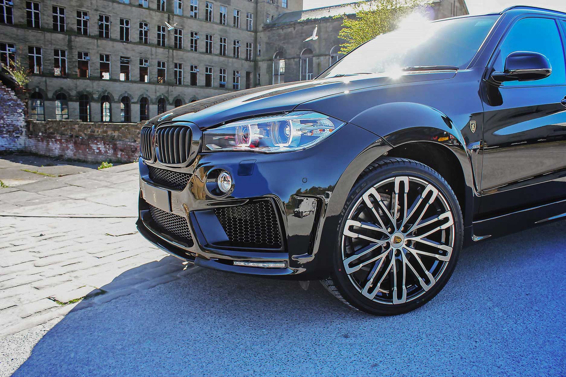 Front quarter detail view of a Black BMW X5 F15 2013-2018. Shot outside an old mill. Fitted with Barugzai Dawn 22” alloy wheels, in Gloss Black Polished Face.