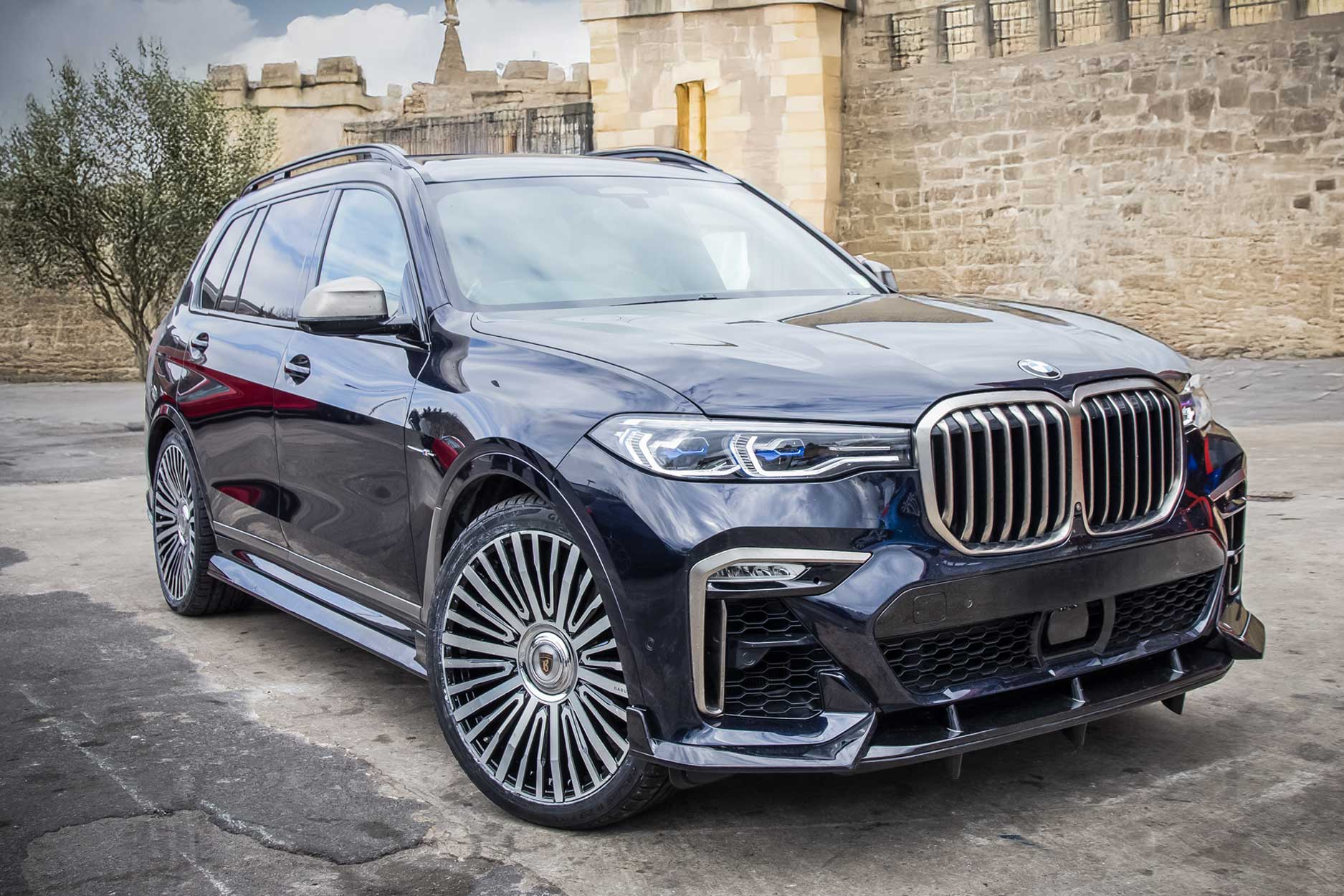 Front quarter view of a Blue BMW X7 G07 2019+. Shot outside a rustic backdrop. Fitted with Barugzai Casanova 22/23” alloy wheels, in Gloss Black Polished Face.
