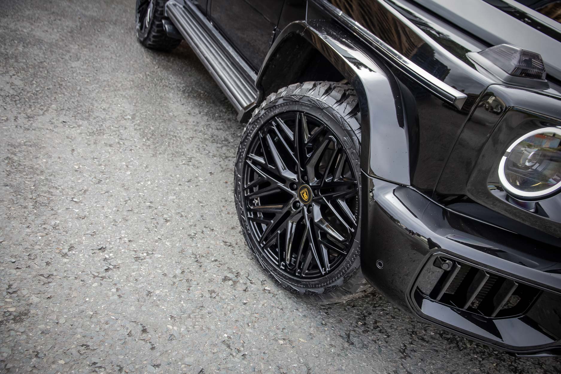 Front quarter detail view of a Black Mercedes G Wagon facelifted to 2025 model. Parked outside a pallet yard. Fitted with Barugzai Shuracan 22” alloy wheels, in Gloss Black.
