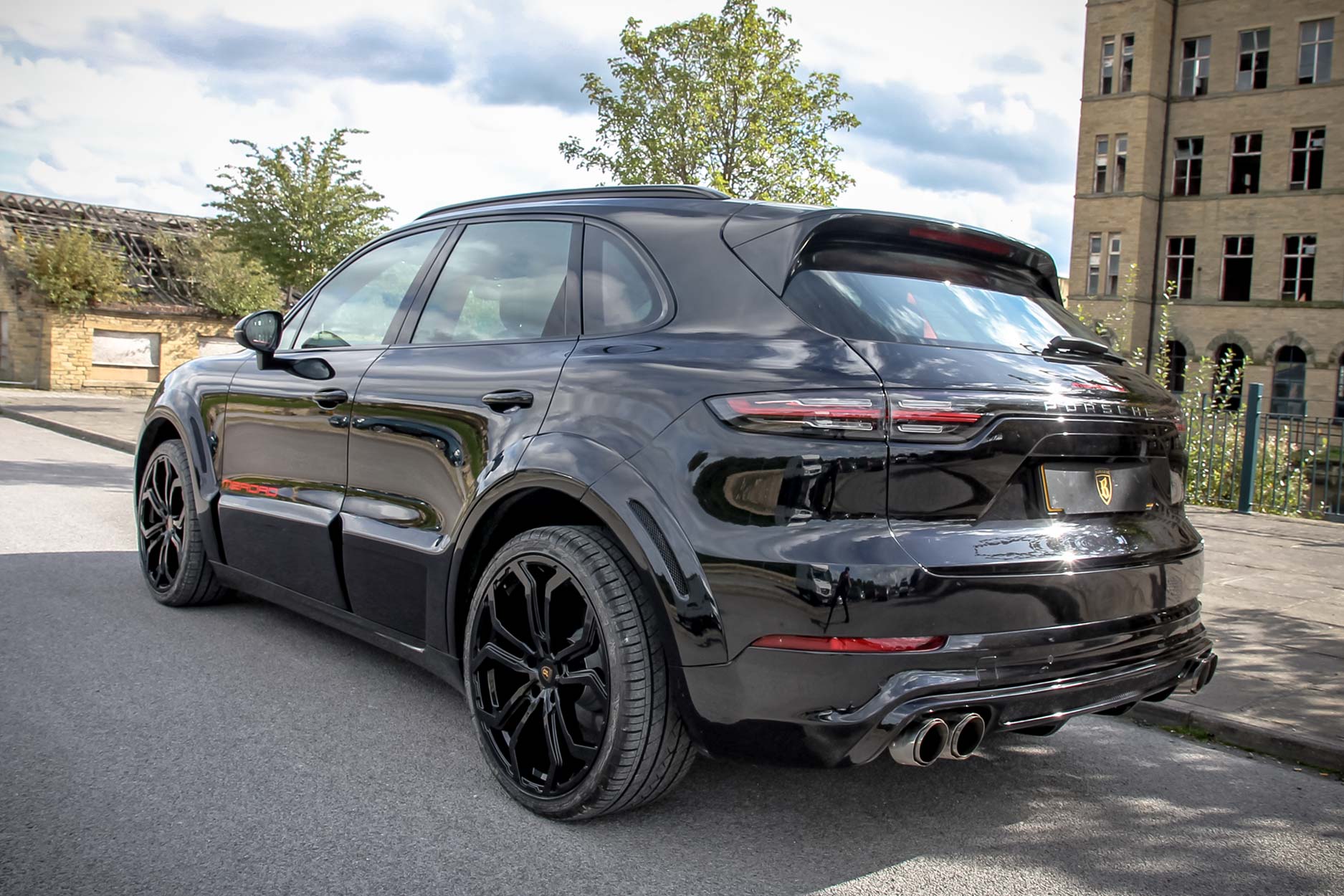 Rear quarter view of a Blue Porsche Cayenne 9YA 2019+ . Shot outside an old mill. Fitted with Barugzai Opium 22” alloy wheels, in Gloss Black