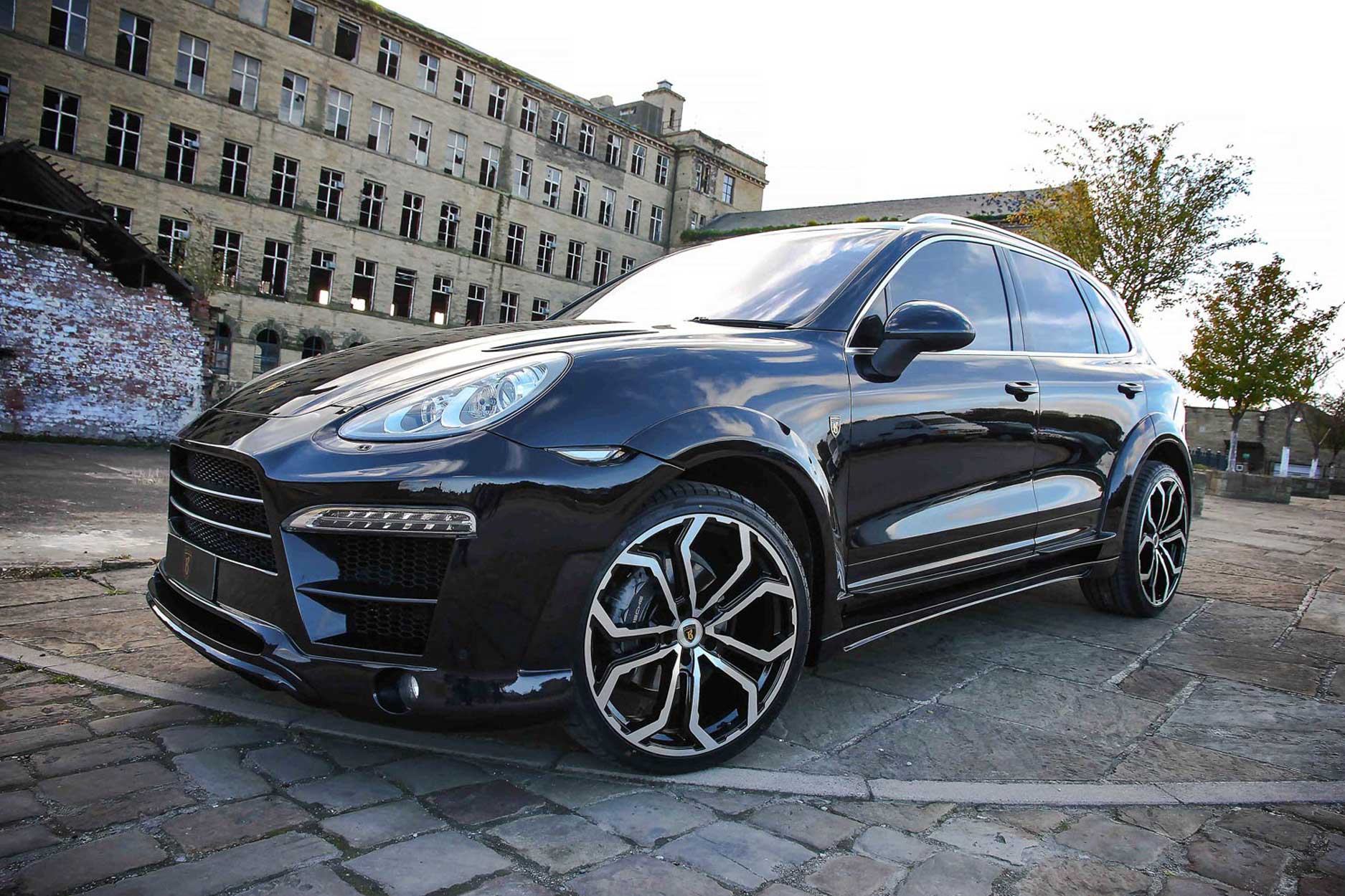 Front quarter view of a Blue Porsche Cayenne 92A 2011-2018. Shot outside an old mill. Fitted with Barugzai Opium 22” alloy wheels, in Gloss Black Polished Face.