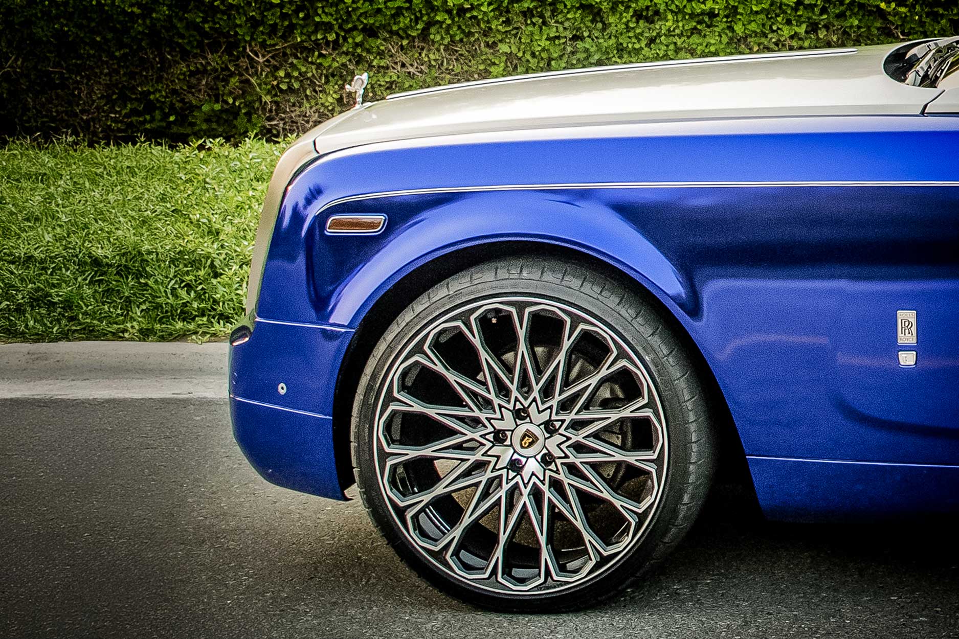Side detail view of a Blue Rolls Royce Phantom Drophead 2007-2016. Shot outside a luxurious mansion. Fitted with Barugzai Majestic 24” alloy wheels, in Gloss Black Polished Face.