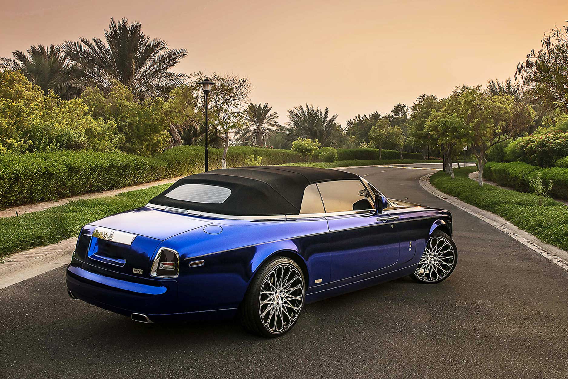 Rear quarter view of a Blue Rolls Royce Phantom Drophead 2007-2016. Shot outside a luxurious mansion. Fitted with Barugzai Majestic 24” alloy wheels, in Gloss Black Polished Face.