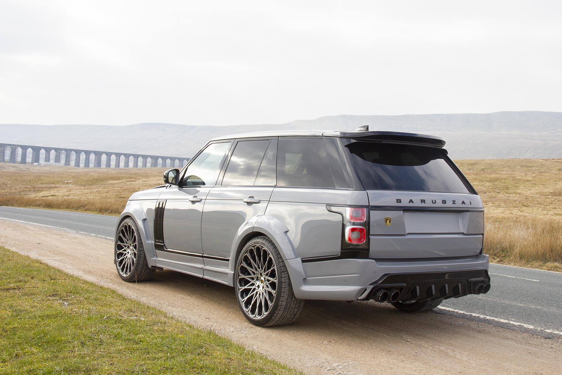 Rear quarter view of a Nardo Grey Range Rover Sport L405 2018-2021. Shot outside a Via Duct. Fitted with Barugzai Majestic 24” alloy wheels, in Gloss Black Polished Face.
