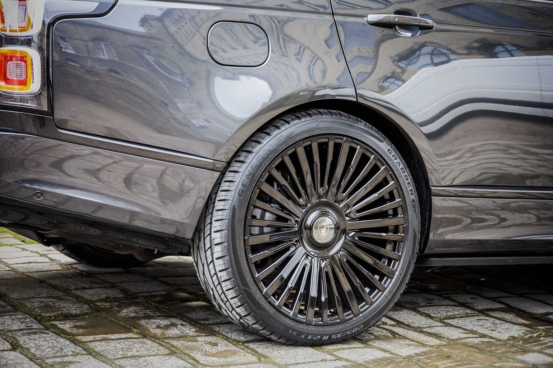 Rear quarter view of a Carpathian Grey Range Rover Vogue L405 SVO style 2018-2021. Shot outside an old mill. Fitted with Barugzai Casanova 22/23” alloy wheels, in Gloss Black