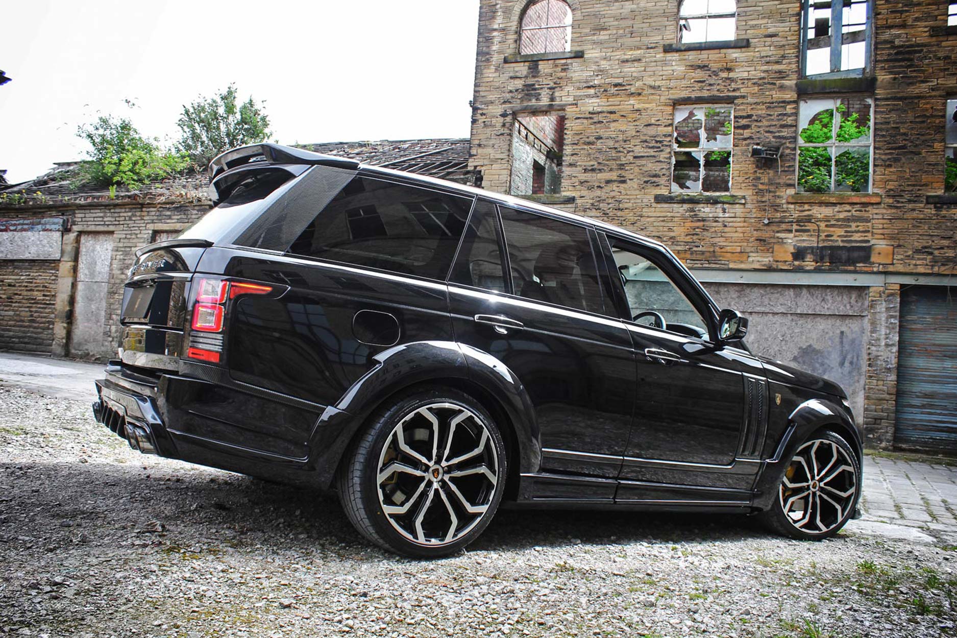 Rear quarter view of a Black Range Rover Vogue L405 2013-2017. Shot outside an old mill. Fitted with Barugzai Opium 22” alloy wheels, in Gloss Black Polished Face.