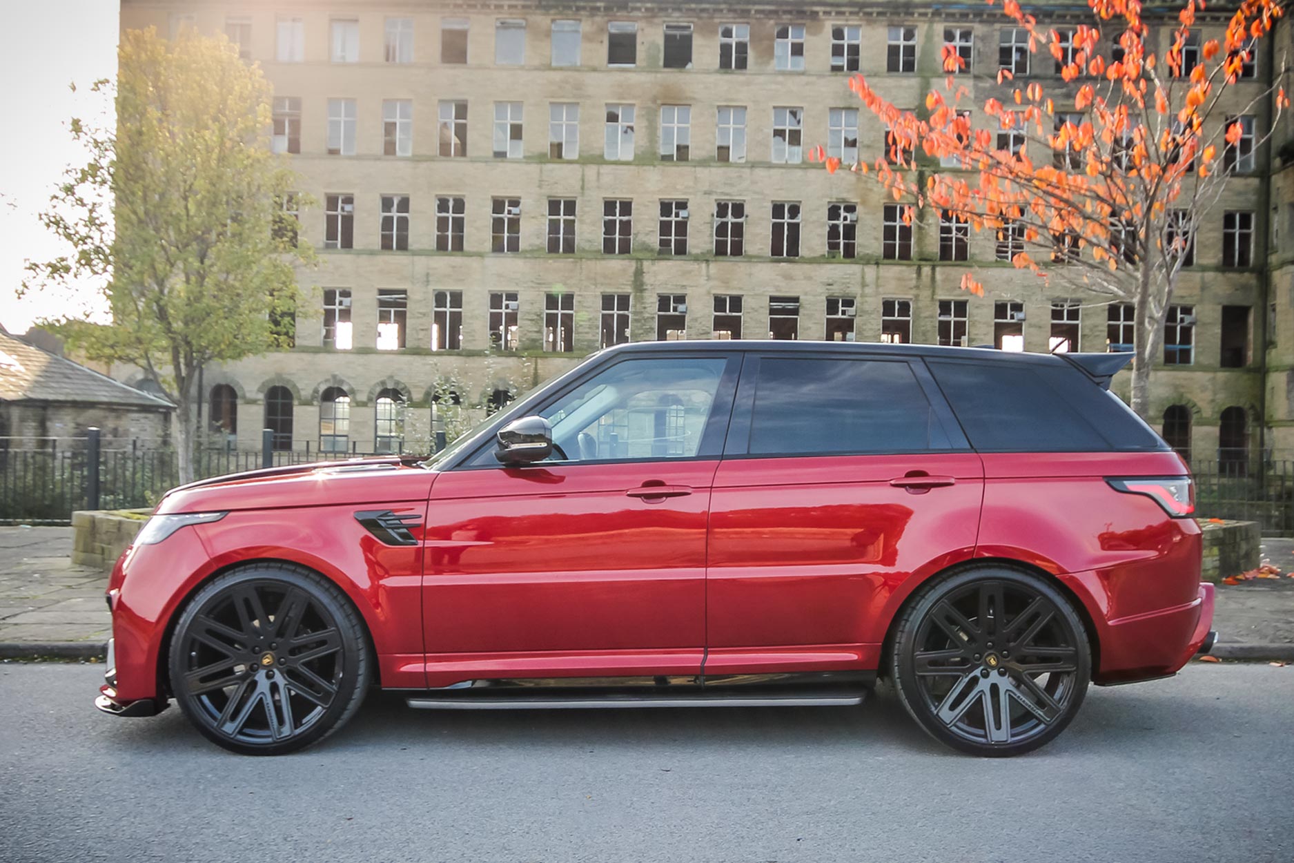 Side view of a Red Range Rover Sport L494 2018-2022. Shot outside an old mill. Fitted with Barugzai EXEL 24” alloy wheels, in Gloss Black.
