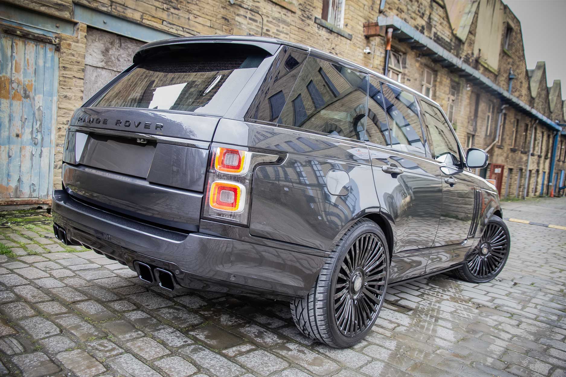 Rear quarter view of a Carpathian Grey Range Rover Vogue L405 SVO style 2018-2021. Shot outside an old mill. Fitted with Barugzai Casanova 22/23” alloy wheels, in Gloss Black