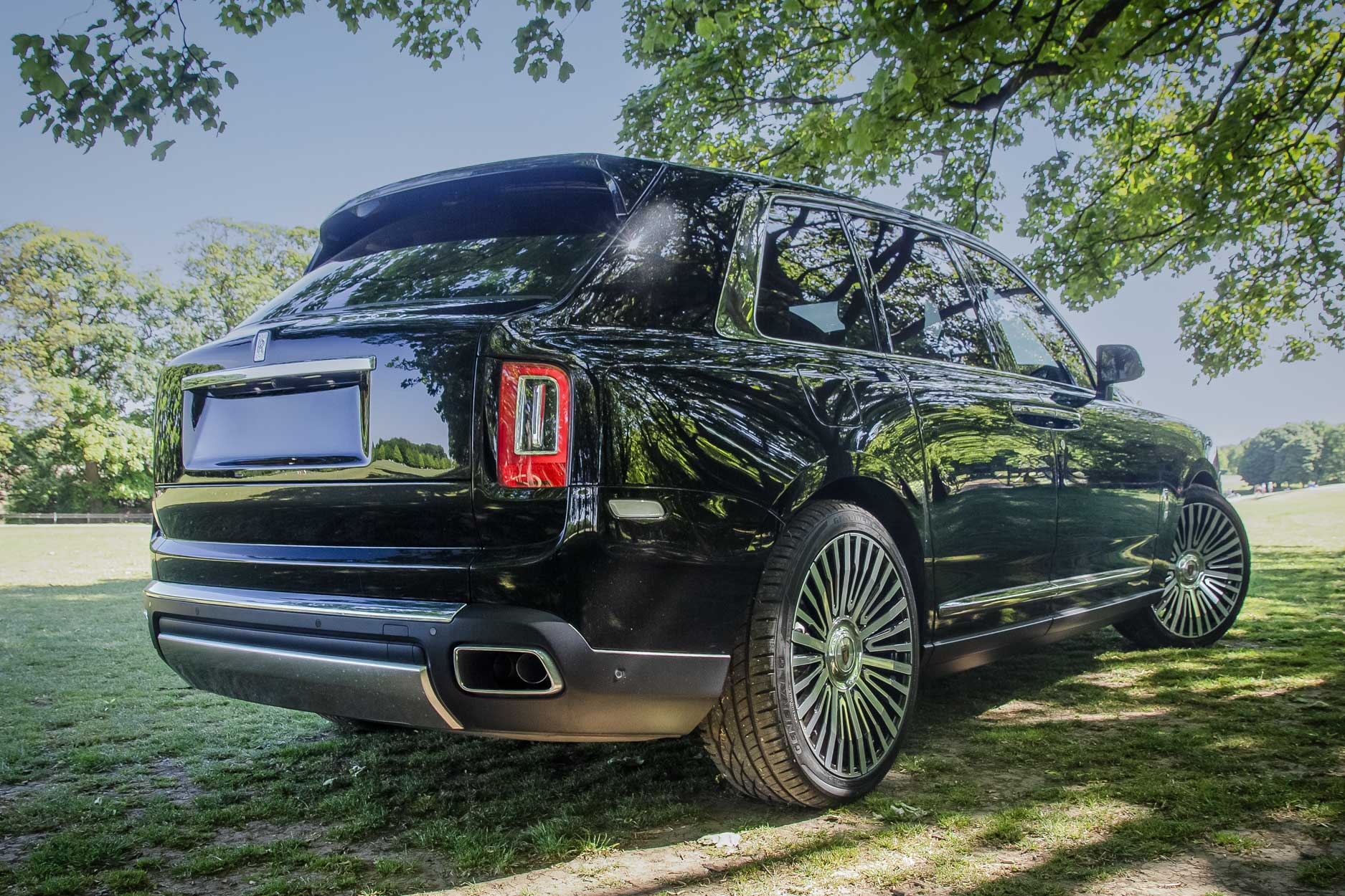 Rear quarter view of a Black Rolls Royce Cullinan 2018+. Shot outside a large lawn backdrop. Fitted with Barugzai Casanova 22/23” alloy wheels, in Gloss Black Polished Face.