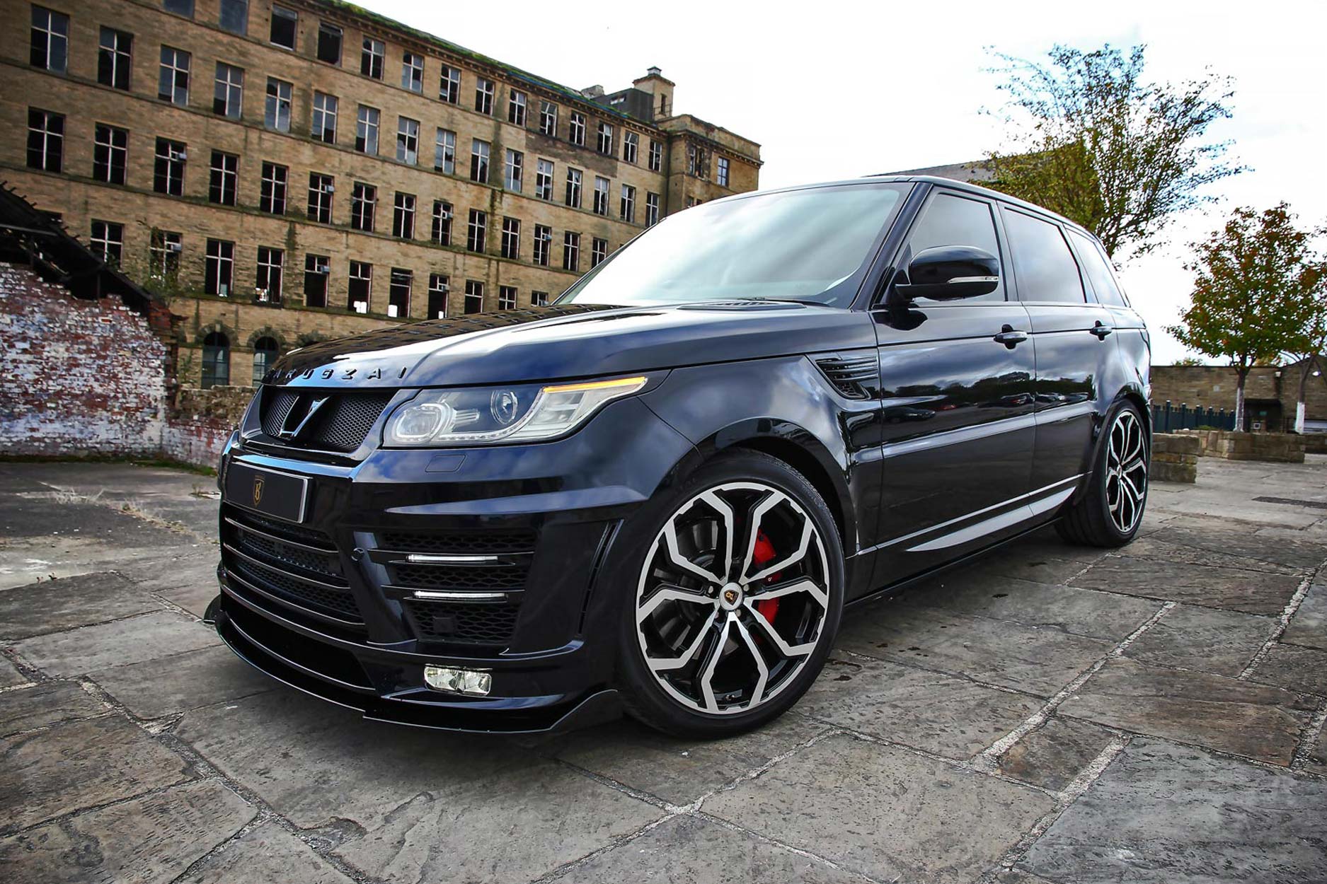 Front quarter view of a Black Range Rover Sport L494 2013-2017. Shot outside an old mill. Fitted with Barugzai Opium 22” alloy wheels, in Gloss Black Polished Face.