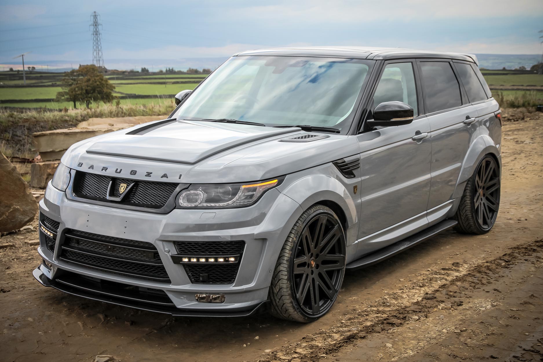 Front quarter view of a Nardo Grey Range Rover Sport L494 2013-2017. Shot outside a quarry. Fitted with Barugzai EXEL 24” alloy wheels, in Gloss Black.