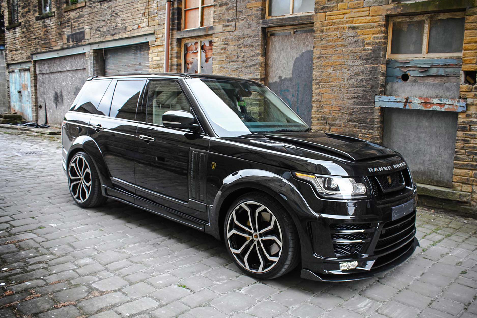 Side quarter detail view of a Black Range Rover Vogue L405 2013-2017. Shot outside an old mill. Fitted with Barugzai Opium 22” alloy wheels, in Gloss Black Polished Face.