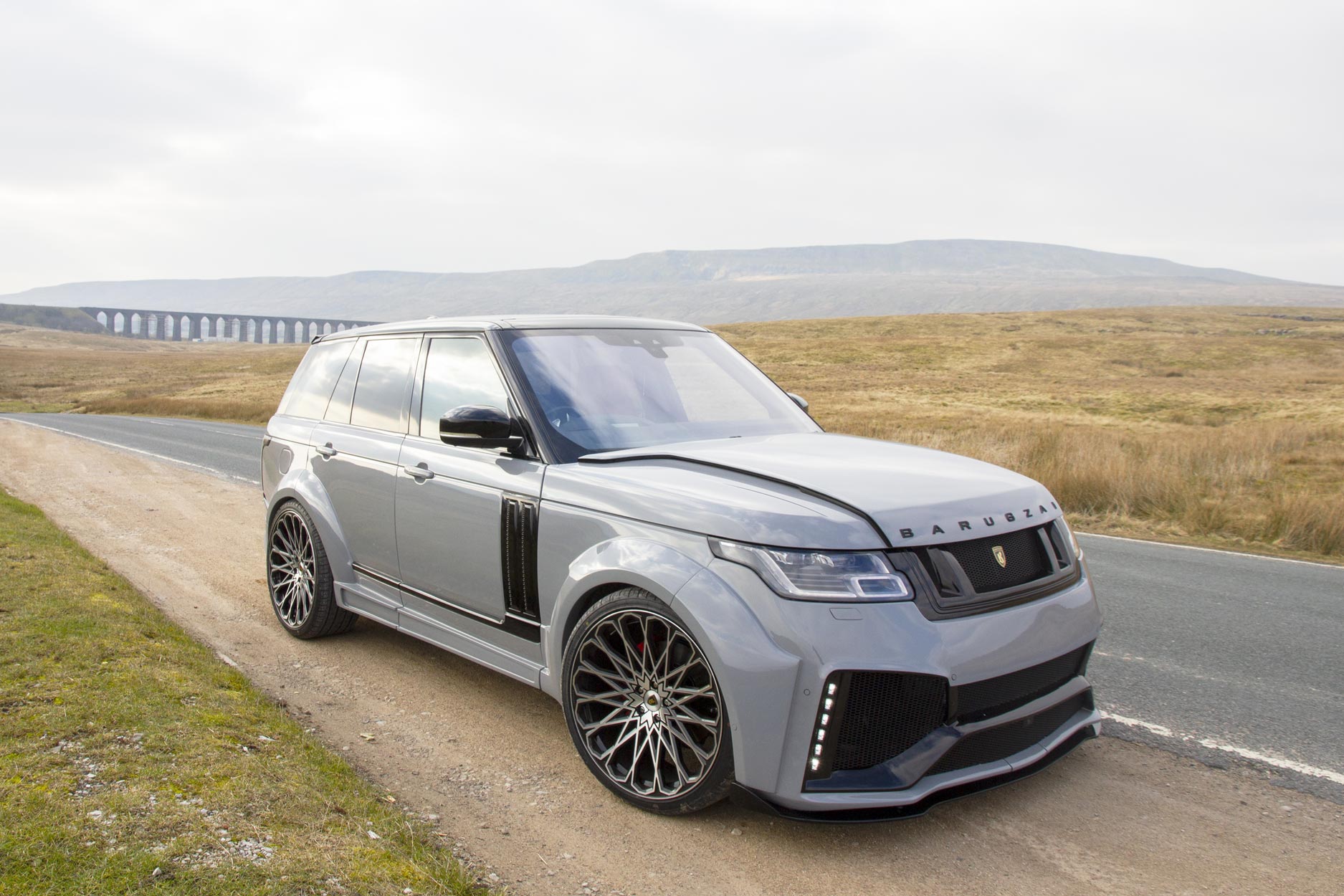 Front quarter view of a Nardo Grey Range Rover Sport L405 2018-2021. Shot outside a Via Duct. Fitted with Barugzai Majestic 24” alloy wheels, in Gloss Black Polished Face.