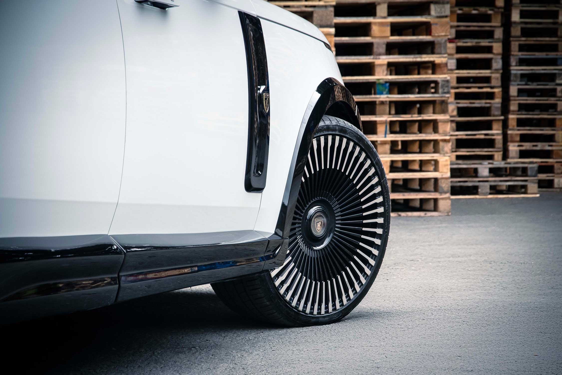 Side quarter detail view of a White Range Rover L460 2022+. Shot outside a pallet yard. Fitted with Barugzai Vortex Forged 24” alloy wheels, in Gloss Black Polished Face.