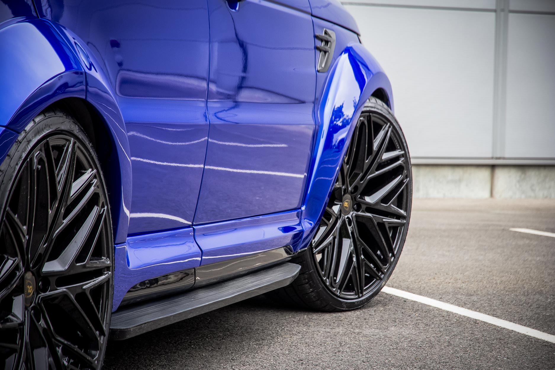 Side quarter detail view of a Blue Range Rover Sport L494 2018-2022. Parked on a road with a grey background. Fitted with Barugzai Shuracan 24” alloy wheels, in Gloss Black.