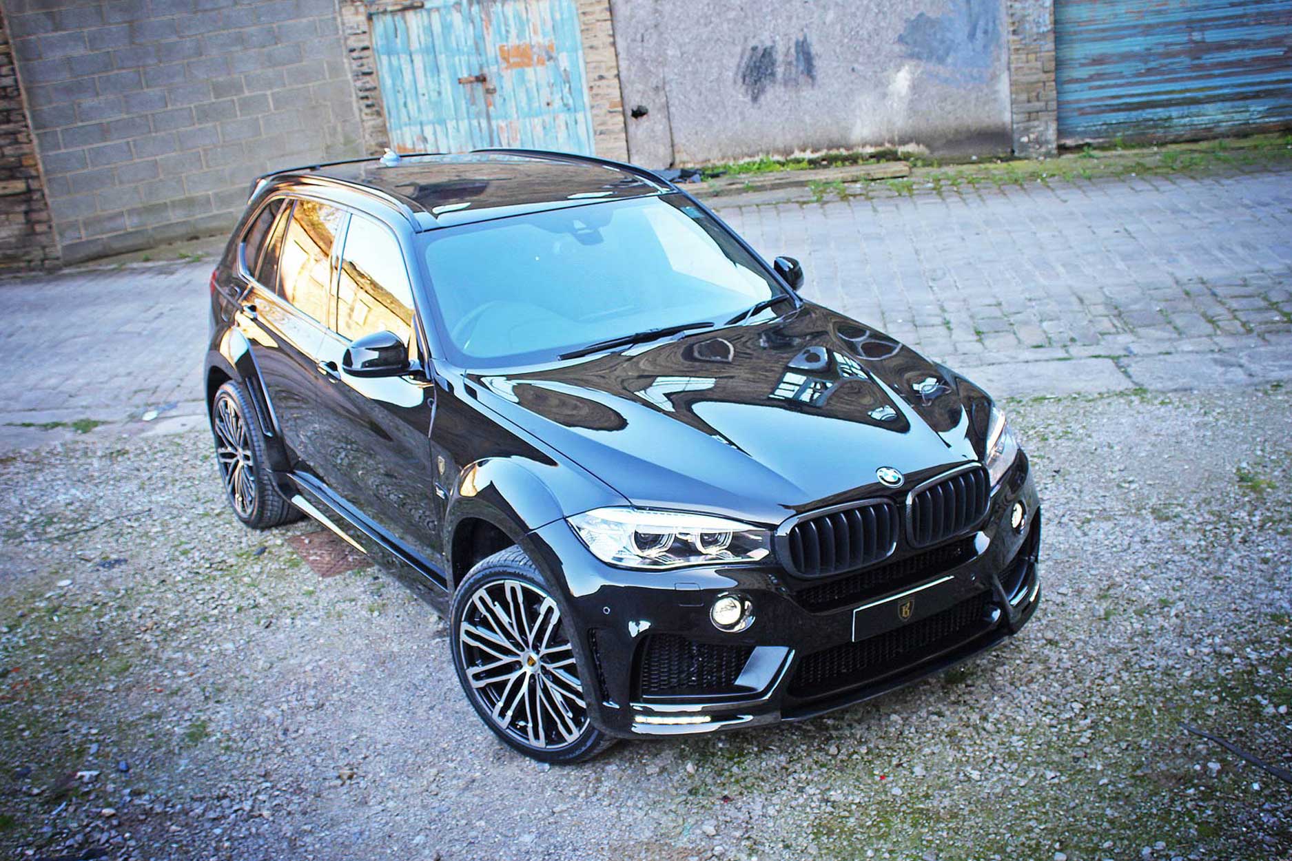 Front quarter view of a Black BMW X5 F15 2013-2018. Shot outside an old mill. Fitted with Barugzai Dawn 22” alloy wheels, in Gloss Black Polished Face.