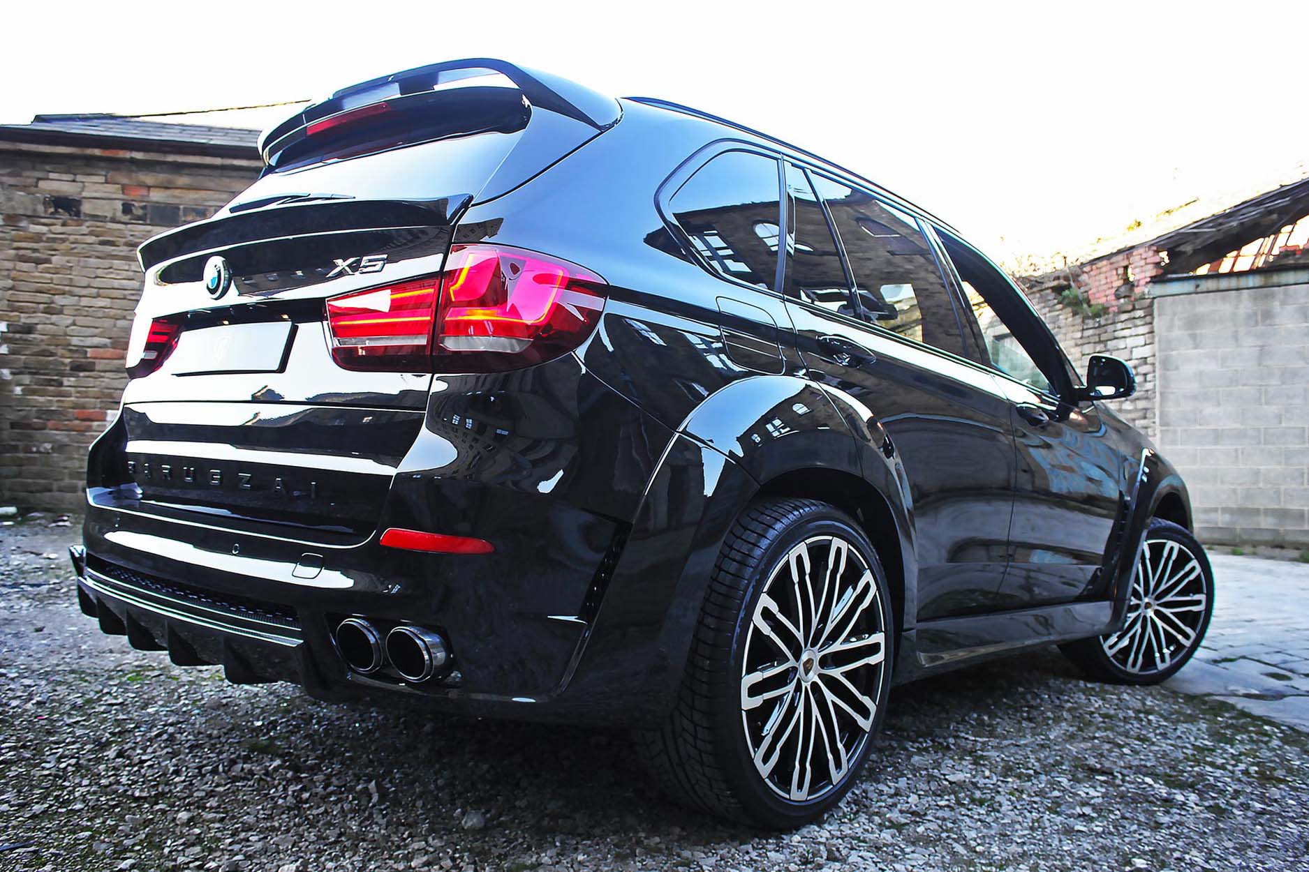 Rear quarter view of a Black BMW X5 F15 2013-2018. Shot outside an old mill. Fitted with Barugzai Dawn 22” alloy wheels, in Gloss Black Polished Face.