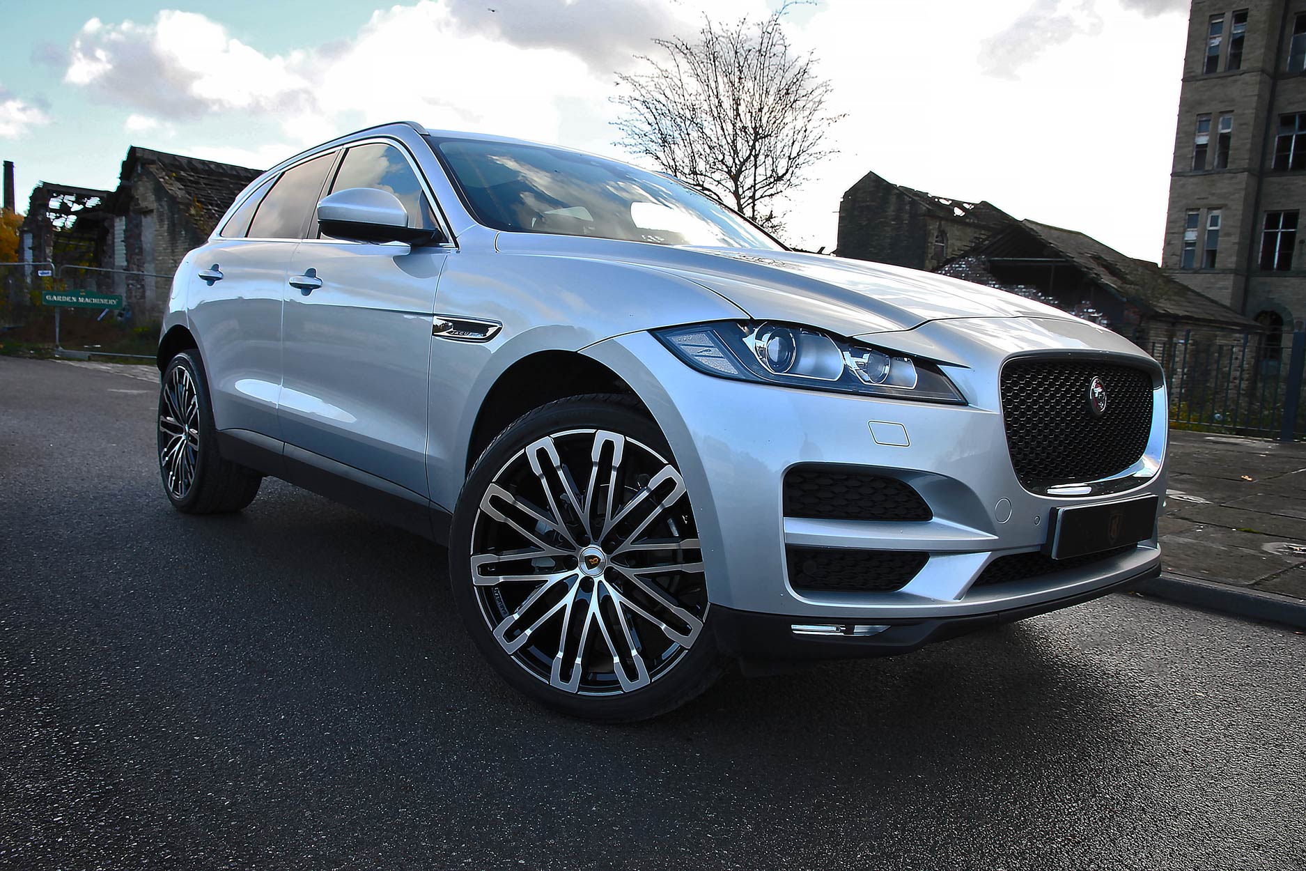 Front quarter view of a Silver Jaguar F-Pace 2016+. Shot outside an old mill. Fitted with Barugzai Dawn 22” alloy wheels, in Gloss Black Polished Face.