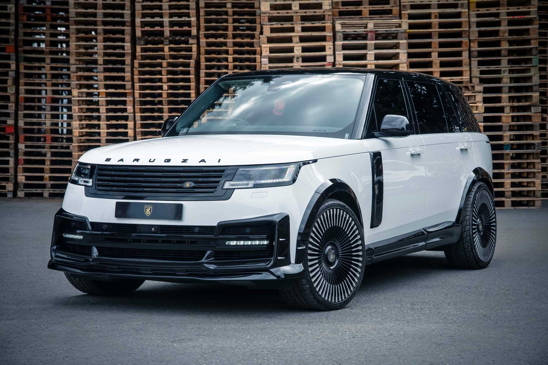 Front quarter view of a White Range Rover L460 2022+. Shot outside a pallet yard. Fitted with Barugzai Vortex Forged 24” alloy wheels, in Gloss Black Polished Face.