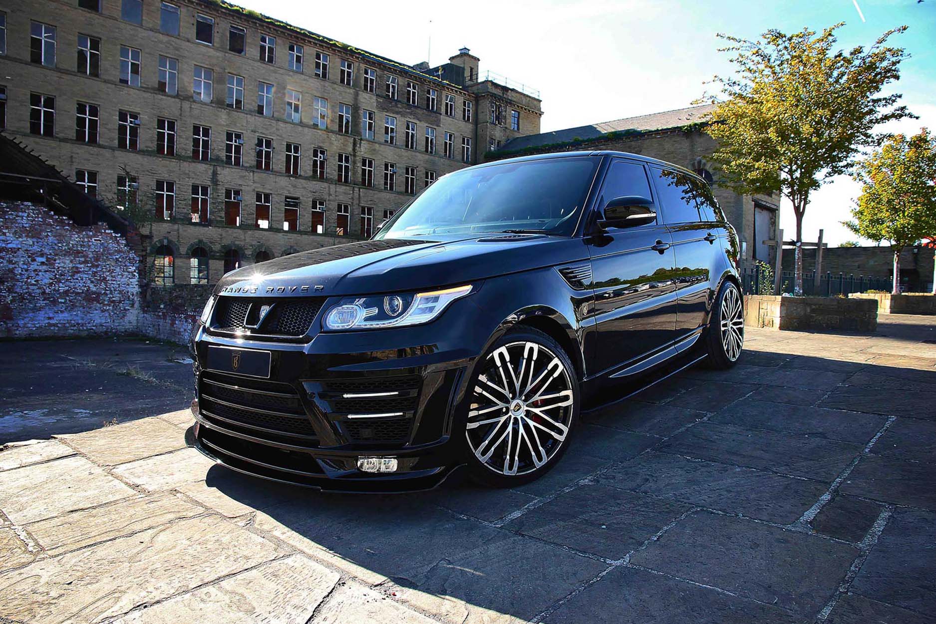 Front quarter view of a Black Range Rover Sport L494 2013-2017. Shot outside an old mill. Fitted with Barugzai Dawn 22” alloy wheels, in Gloss Black Polished Face.