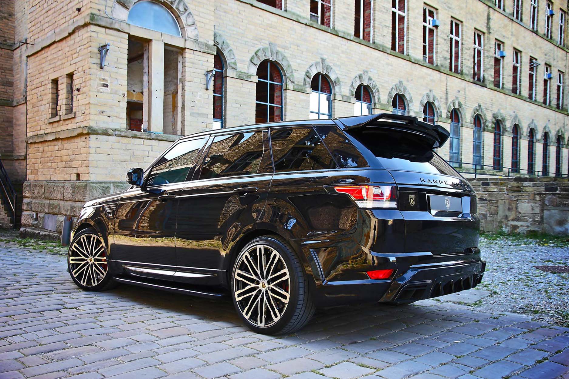 Rear quarter view of a Black Range Rover Sport L494 2013-2017. Shot outside an old mill. Fitted with Barugzai Dawn 22” alloy wheels, in Gloss Black Polished Face.