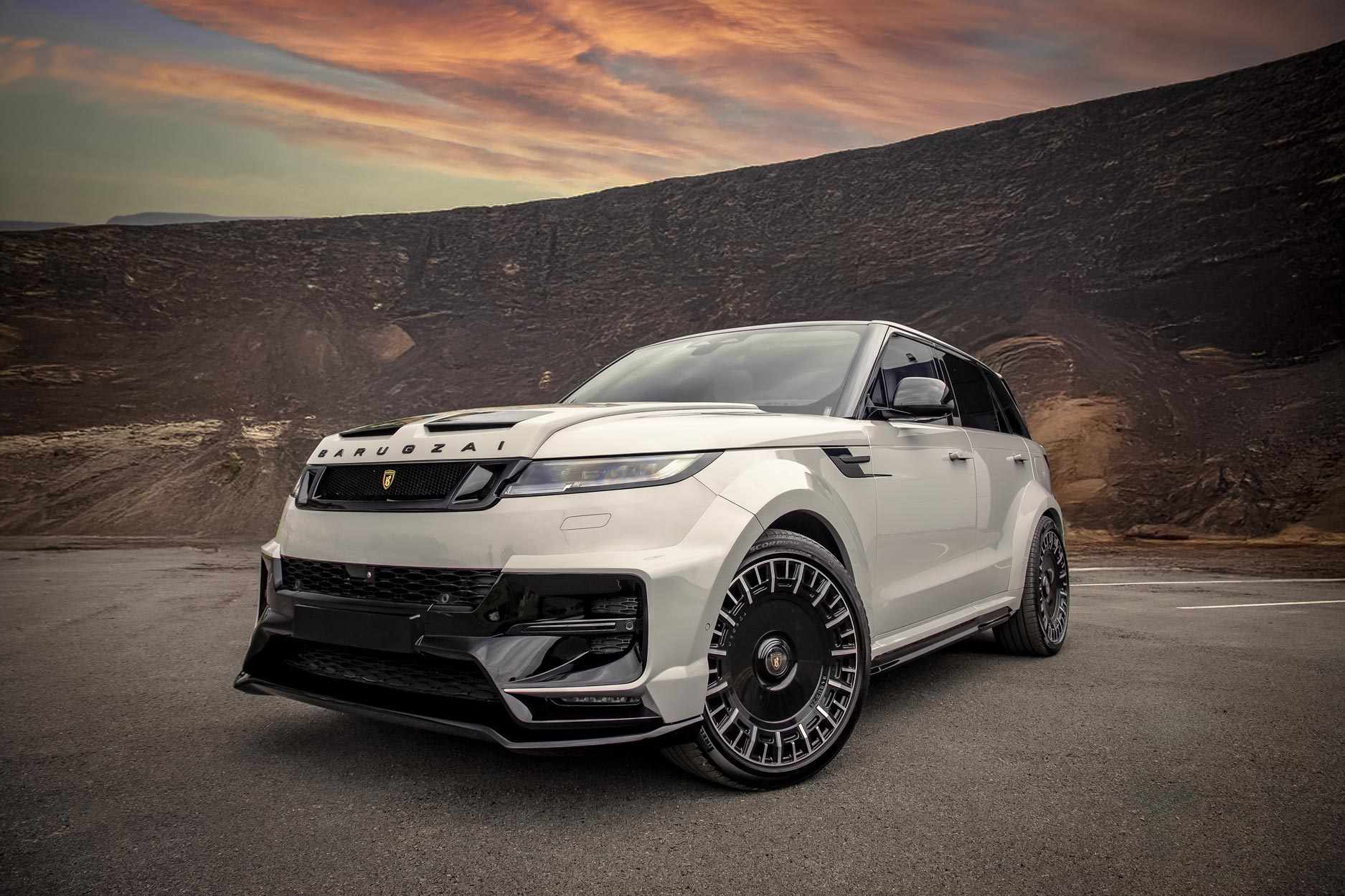 Front quarter view of a Nardo Grey Range Rover Sport L461 2023+. Shot outside a mountainous backdrop. Fitted with Barugzai Monoblok 23” alloy wheels, in Gloss Black Polished Face.