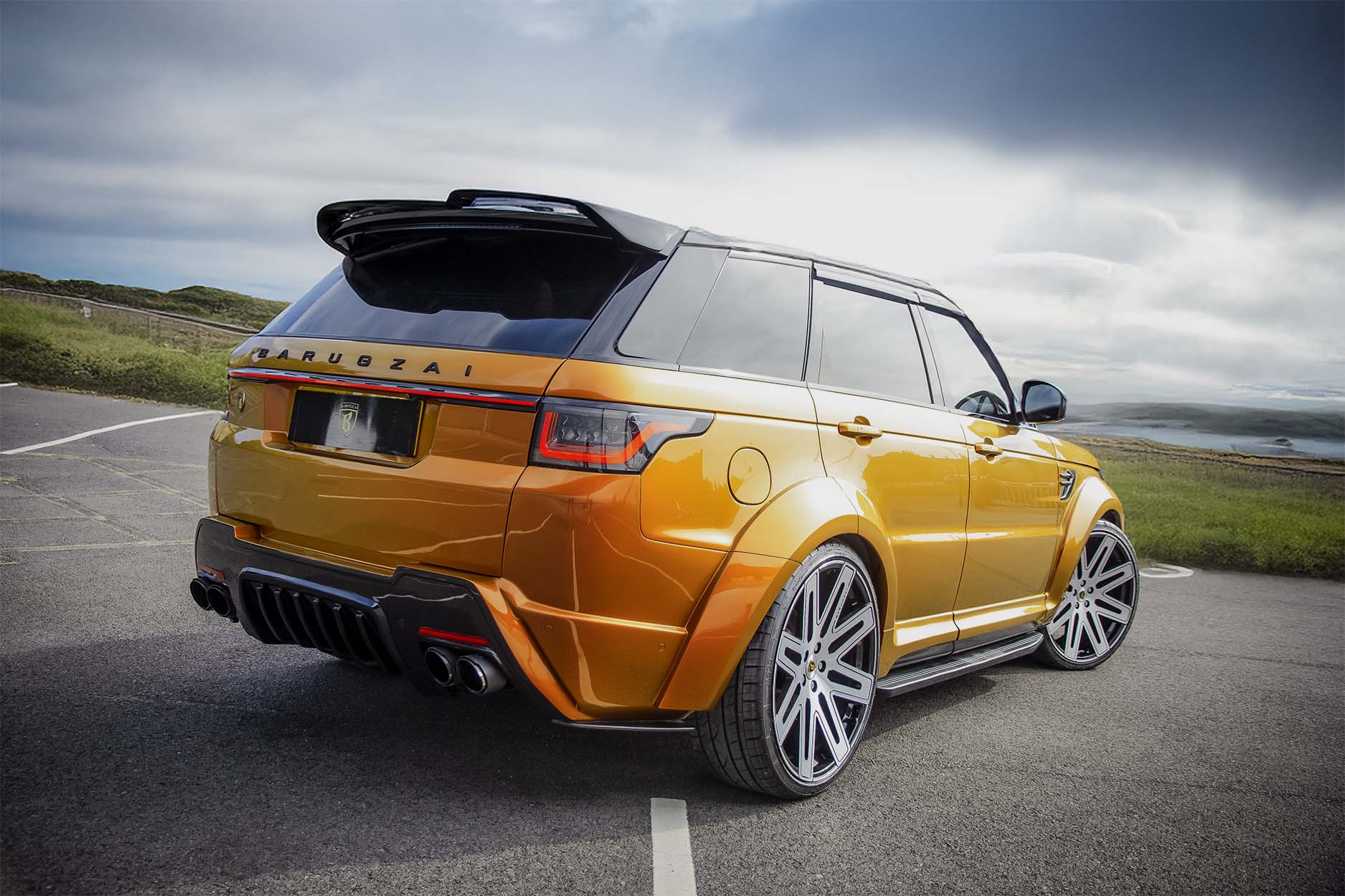 Rear quarter detail view of an Orange Range Rover Sport L494 2018-2022. Shot outside a scenic backdrop. Fitted with Barugzai EXEL 24” alloy wheels, in Gloss Black Polished Face.