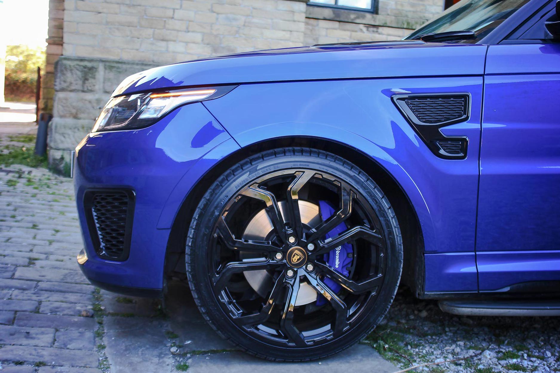 Side detail view of a Blue Range Rover Sport SVR L494 2013-2017. Shot outside an old mill. Fitted with Barugzai Opium 22” alloy wheels, in Gloss Black
